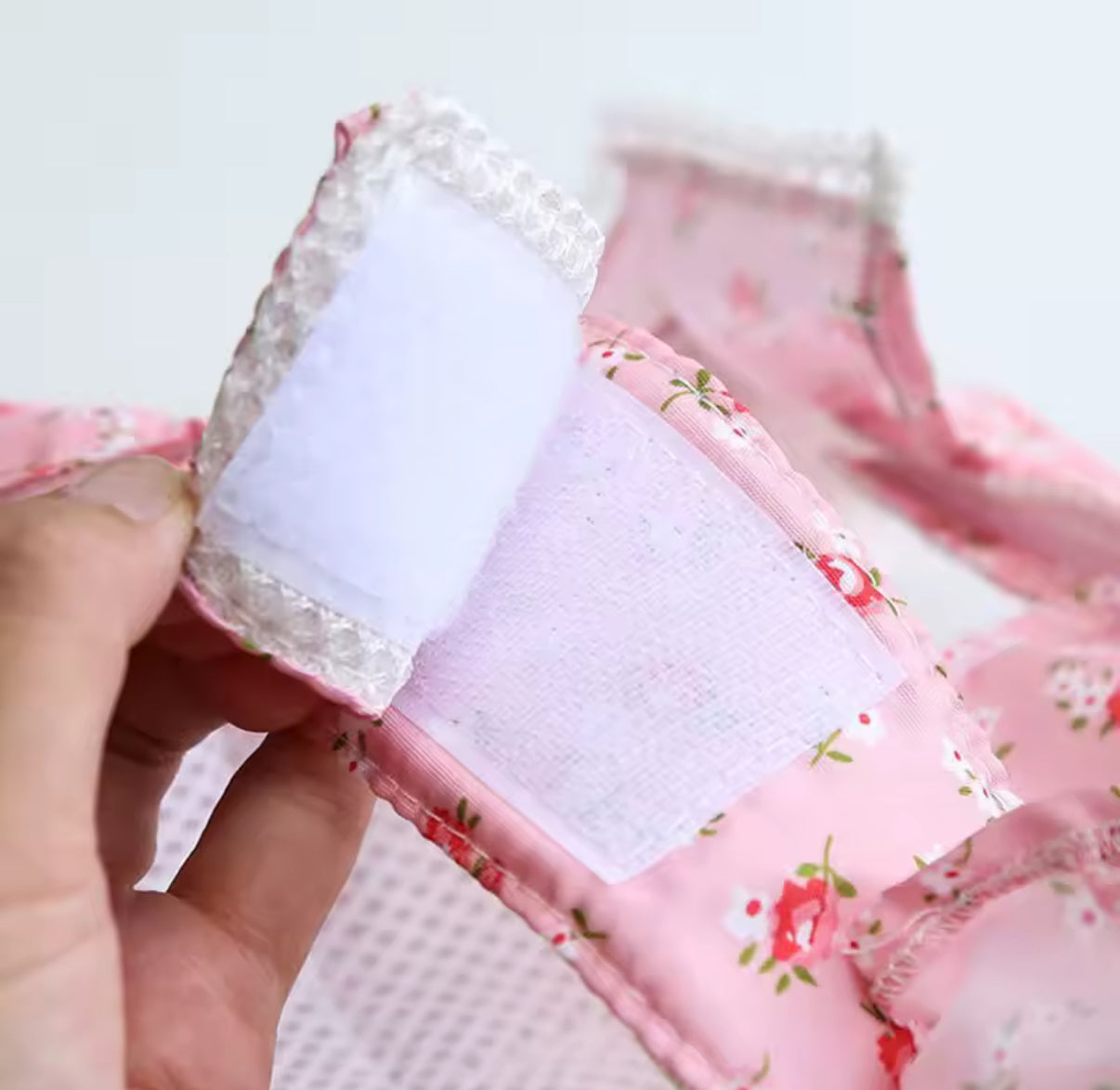 Close-up of a pink floral fabric with white lace trim held by a hand against a light background.